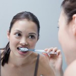 Young woman looking in the mirror and brushing her teeth.