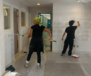 Two people painting a plain wall with white primer.