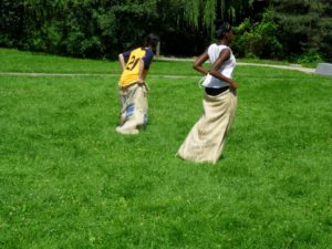 Two youth participating in a sack race outside on green grass.