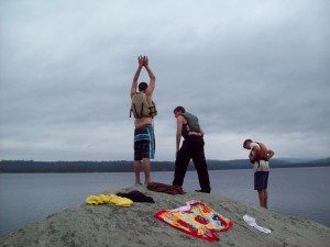 Young people on a rock overlooking a body of water in overcast weather.