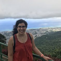 A young woman standing on a high hill overlooking a city and some greenery.